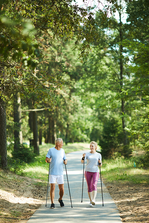 Aged spouses in activewear trekking along road in park among green trees on summer weekend