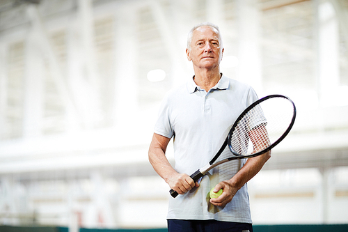 Aged tennis player in activewear standing inside large stadium or modern sports center