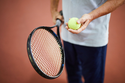 Light green tennis ball in hand of aged tennis player and racket in the other one