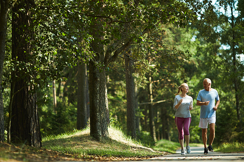 Healthy active senior couple in sportswear running among green trees on sunny day in summer