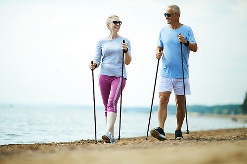 Happy active aged couple trekking along coastline on sandy beach in the morning