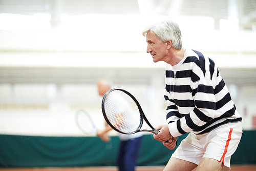 Aged tennis player in activewear holding racket while concentrating on ball movement during game