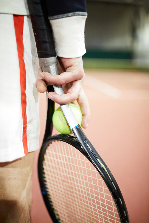 Hand of professional tennis player holding ball and racket while standing on stadium