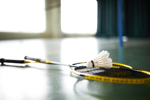 White badminton shuttlecock and two rackets on the floor of modern leisure hall or sports center