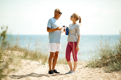 Couple of retired man and woman having water and discussing their success in morning trainings