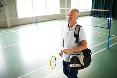 Senior grey-haired active man with sportsbag and racket leaving leisure center after playing badminton