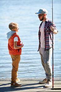 Young man with fishing rod talking to his son while both standing on pontoon