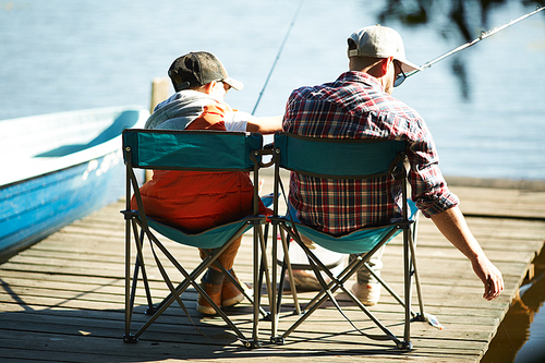 Rear view of father and son fishing together on a pier in summer day