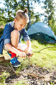 Young scout trying to make campfire on green glade in the forest during trip