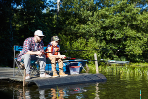 Dad and son fishing at lake in the countryside, they sitting with fishing rods and waiting for catch