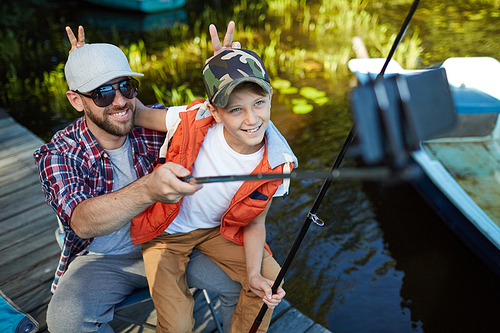 Father and son posing to the camera on smartphone while making selfie portrait during fishing