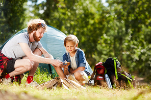 young scout showing his son how to make campfire during trip in natural