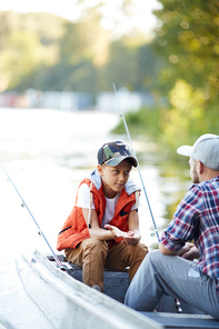 Little boy asking or explaining something to his dad while both sitting in boat during fishing