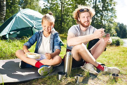 two young trippers sitting on ground in natural  and having breakfast in the morning
