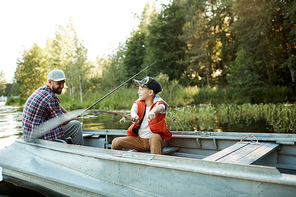 Happy little boy with rod showing his father where the fish is while both sitting in boat