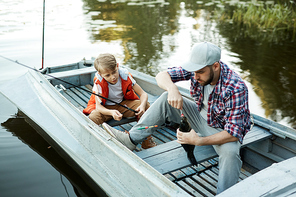 Father fishing on the boat together with his son, they are catching a big fish