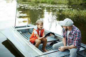 Joyful boy showing his father big fish that he caught while sitting and talking in boat