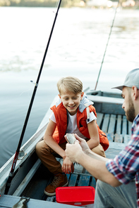 Young man showing his son fish and pointing out its appearance during their conversation in boat