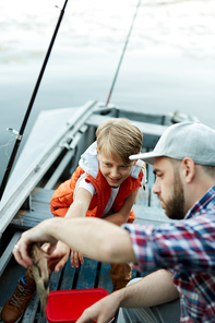 Father and son catching a fish while they fishing on the boat on the lake