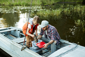 Little boy outting big fish into plastic bucket or container during fishing with father