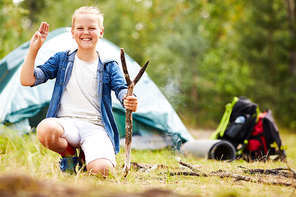 Young boy scout with stick showing open palm and three fingers put together during his backpack trip