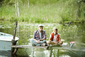 Father and son sitting on pontoon with their rods in water and waiting for fish