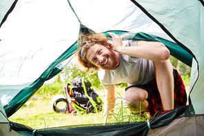 happy young man looking into tent while enjoying his trip on summer weekend in natural