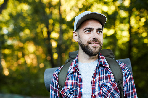 Young cheerful man with backpack hiking in the forest