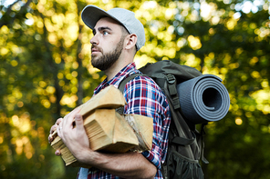 Young man with backpack and stack of firewood going to make campfire after long trip
