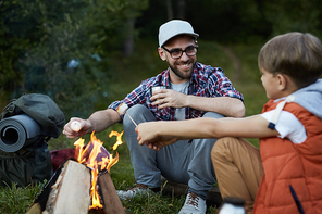 Dad and son are heated by the fire, eat marshmallows and drink hot tea