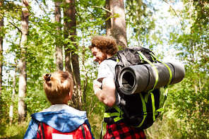 Father and son scouts with backpacks walking in the forest to their camp on sunny day