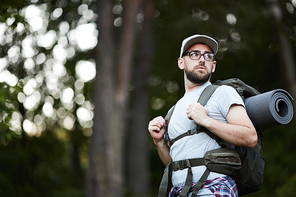 Young man wearing eyeglasses in backpack travelling through the forest