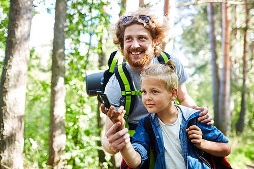 Happy young man and his son with compass orienting in the forest during trip