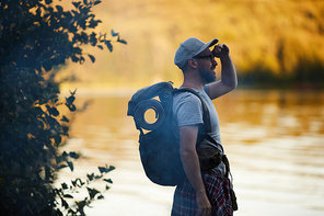 Young tourist with backpack standing near the lake and looking at view