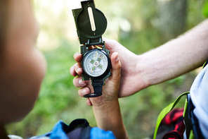 Hands of boy scouts holding compass with arrow pointing north while looking for their camp