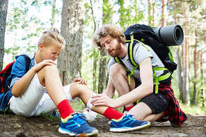 Young scout helping his friend with bandage to bind up injury on leg on their way to camp