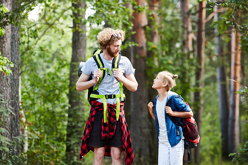 Young man and boy with backpacks having talk while walking to their camp of scouts