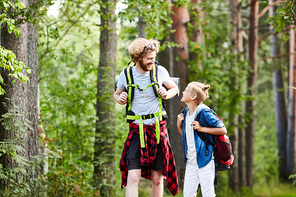 Two friendly boy scouts with backpacks walking in the forest and having talk on their way to camp