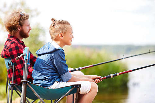 Father and son with rods fishing together by lake on summer weekend