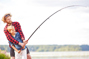 little boy and his father holding fishing rod over lake while spending summer weekend in natural