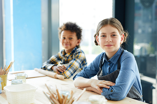 Two young diligent intercultural pupils sitting by desk in studio of crafts and 