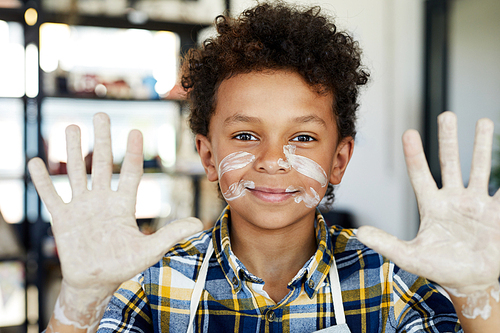 Cute happy boy with mud on his palms and face showing hands dirty after work with clay