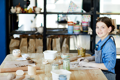 Happy creative schoolgirl  while sitting by table at lesson of creative crafts