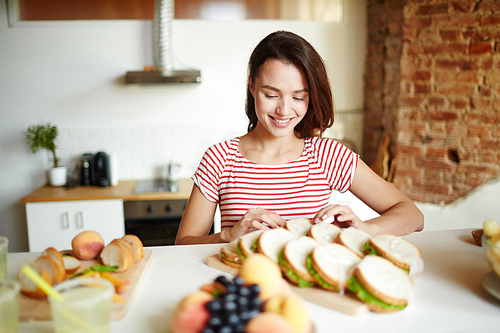 Pretty young housewife making tasty sandwiches in the kitchen for guests