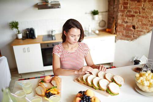 Attractive young woman putting homemade sandwiches in two rows on wooden board