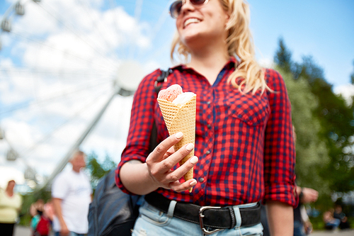 Yummy double-topping icecream in hand of casual blond girl visiting modern amusement park on summer day