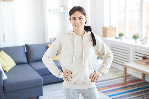 Young sporty woman in activewear looking at you while exercising at home
