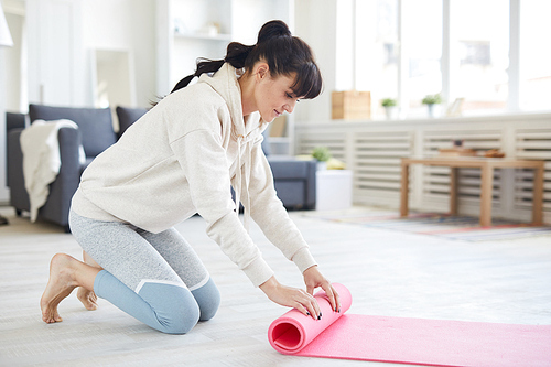 Young woman in activewear rolling pink mat in after workout in living-room