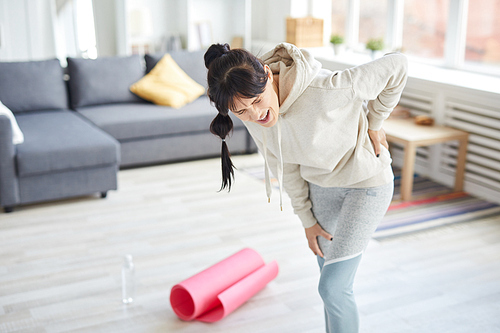 Young sportswoman feeling pain in her back after workout and touching where it hurts