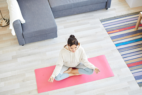 Overview of young sporty female in activewear sitting in pose of lotus on mat while exercising